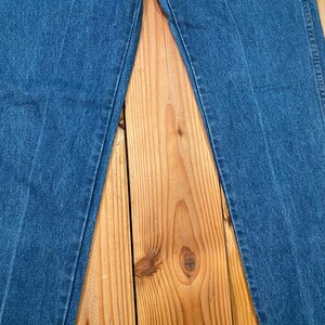 May include: Close-up of blue denim jeans. The jeans are laid flat on a wooden surface, showcasing the texture and stitching details. The denim has a classic, medium-wash appearance.