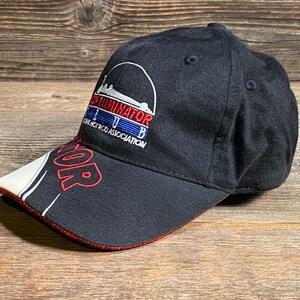 May include: Black baseball cap with the word "TERMINATOR" in red on the brim. The cap features a white and red design on the brim and the text "TERMINATOR IHB HOT ROD ASSOCIATION" in white, red, and blue.