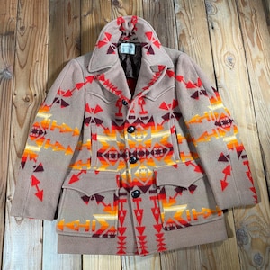 Peut inclure: Une veste en laine beige ornée d'un motif géométrique vif dans des tons de rouge, orange et jaune. La veste présente un large col, des manches longues, trois boutons noirs sur le devant et deux poches à rabat à la taille avec une doublure marron.