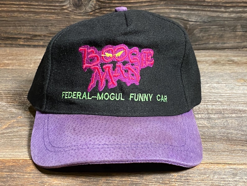 May include: Black baseball cap with a purple brim and top button. The cap features the embroidered text "Boogie Man" in pink with yellow accents, and "FEDERAL-MOGUL FUNNY CAR" in green.