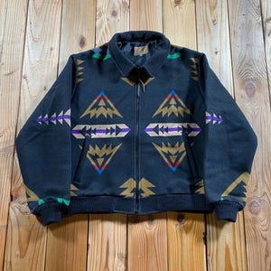 Puede incluir: Una chaqueta negra con cremallera y un llamativo patrón geométrico en tonos beige, azul, morado y verde. La chaqueta cuenta con cuello vuelto, mangas largas con puños acanalados, dobladillo acanalado, dos bolsillos frontales y cierre central.