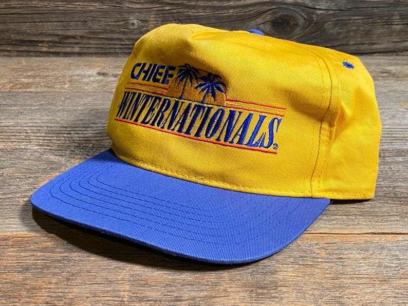 May include: A yellow baseball cap with a blue brim. The cap features the text "CHIEF WINTERNATIONALS" in blue and red, with palm tree graphics. The hat is made of a durable fabric.