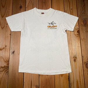 Puede incluir: Camiseta blanquecina con un peque&ntilde;o gr&aacute;fico en la parte delantera. El gr&aacute;fico presenta un pez estilizado y el texto "Mike Fish It's the Attitude" en naranja y negro. La camiseta es de un material suave.