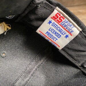 May include: Close-up of a black baseball cap. The interior features a tag with the text "SS Sport Service Officially Licensed Product Made in China". The tag has red and blue accents.