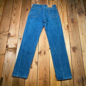 May include: Blue denim jeans with a classic five-pocket design. The jeans are laid flat, showcasing the back pockets and the overall straight-leg cut. The denim has a medium wash, and the jeans appear to be in good condition.