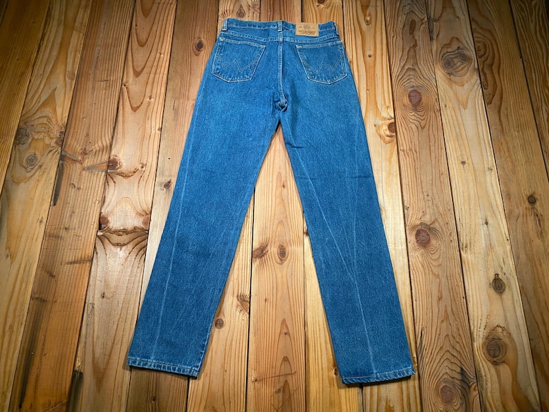 May include: Blue denim jeans with a classic five-pocket design. The jeans are laid flat, showcasing the back pockets and the overall straight-leg cut. The denim has a medium wash, and the jeans appear to be in good condition.