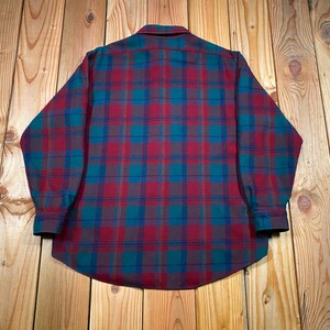 May include: A long-sleeved plaid shirt in a classic pattern. The shirt features a button-down collar and cuffs. The plaid design incorporates shades of burgundy, teal, and navy blue. The shirt is made of a soft, possibly flannel, material.