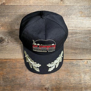 May include: A black baseball cap with embroidered text and design. The text reads "TOP ELIMINATOR NATIONAL HOT ROD ASSOCIATION MEMBERS ONLY". The brim features embroidered green and white leaf designs.