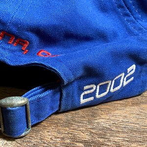 Puede incluir: Gorra de b&eacute;isbol azul con el a&ntilde;o "2002" en letras blancas. La gorra tiene una hebilla ajustable de metal y texto bordado en rojo. La gorra est&aacute; hecha de tela duradera.