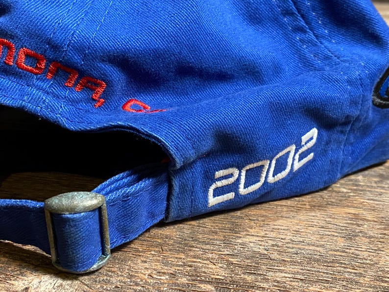 Puede incluir: Gorra de b&eacute;isbol azul con el a&ntilde;o "2002" en letras blancas. La gorra tiene una hebilla ajustable de metal y texto bordado en rojo. La gorra est&aacute; hecha de tela duradera.