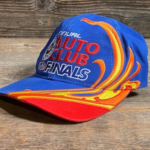 Puede incluir: Gorra de b&eacute;isbol azul con el texto "Annual Auto Club Finals" en rojo y blanco. La gorra presenta un dise&ntilde;o de llama en amarillo y naranja, con una visera roja.