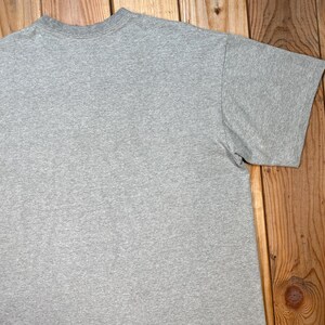 Puede incluir: Una camiseta gris jaspeada de manga corta. La camiseta est&aacute; hecha de un material suave y c&oacute;modo. La camiseta tiene cuello redondo y mangas cortas. La camiseta se muestra sobre una superficie de madera.