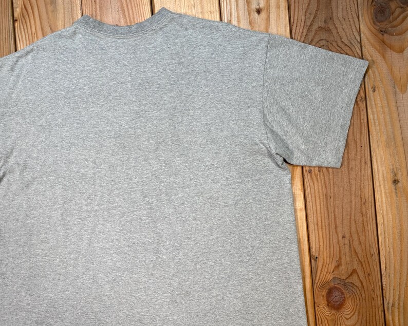 Puede incluir: Una camiseta gris jaspeada de manga corta. La camiseta est&aacute; hecha de un material suave y c&oacute;modo. La camiseta tiene cuello redondo y mangas cortas. La camiseta se muestra sobre una superficie de madera.