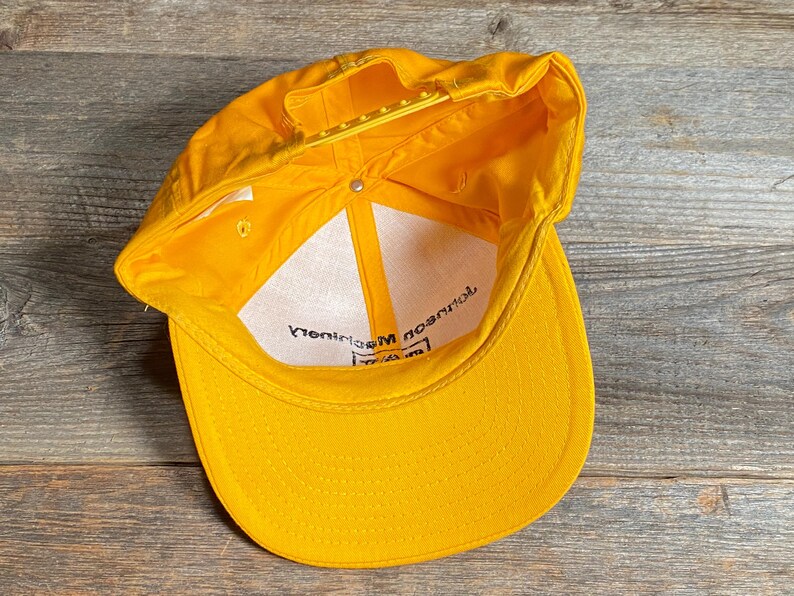 May include: A bright yellow baseball cap with a curved brim and adjustable snapback closure. The interior features a white lining with black text. The cap is made of a durable material and is designed for sun protection.