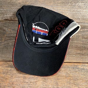 May include: Black baseball cap with red and white accents. The cap features the text "TOP ELIMINATOR CLUB" and "MEMBERS ONLY". The brim has a red trim and the interior is white.
