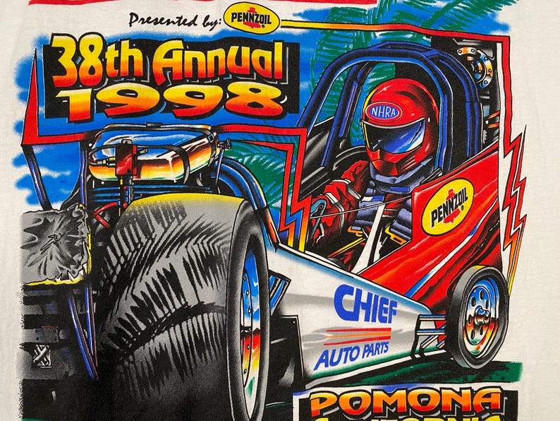 May include: White t-shirt featuring a colorful graphic of a drag racing car. The design includes the text "38th Annual 1998" and logos for Pennzoil, NHRA, and Chief Auto Parts. The car is red and blue with a driver wearing a red helmet.