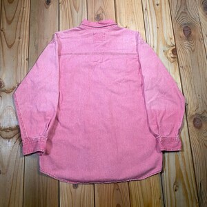 Puede incluir: Una camisa de manga larga con botones en un color rosa s&oacute;lido. La prenda presenta un cuello cl&aacute;sico, un canes&uacute; horizontal en la espalda y pu&ntilde;os abotonados al final de cada manga. La tela tiene una apariencia texturizada con costuras visibles.