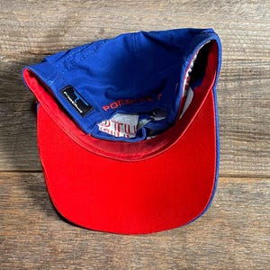 Puede incluir: Gorra de b&eacute;isbol azul con visera roja. La gorra tiene una visera curva y una corona estructurada. El forro interior es blanco con un patr&oacute;n rojo y azul. El texto "POWER" es visible en el lateral.