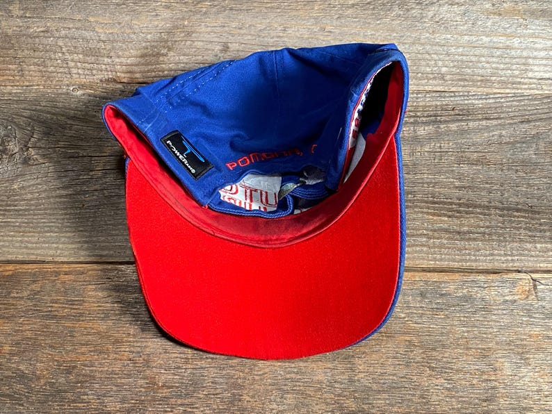 Puede incluir: Gorra de b&eacute;isbol azul con visera roja. La gorra tiene una visera curva y una corona estructurada. El forro interior es blanco con un patr&oacute;n rojo y azul. El texto "POWER" es visible en el lateral.