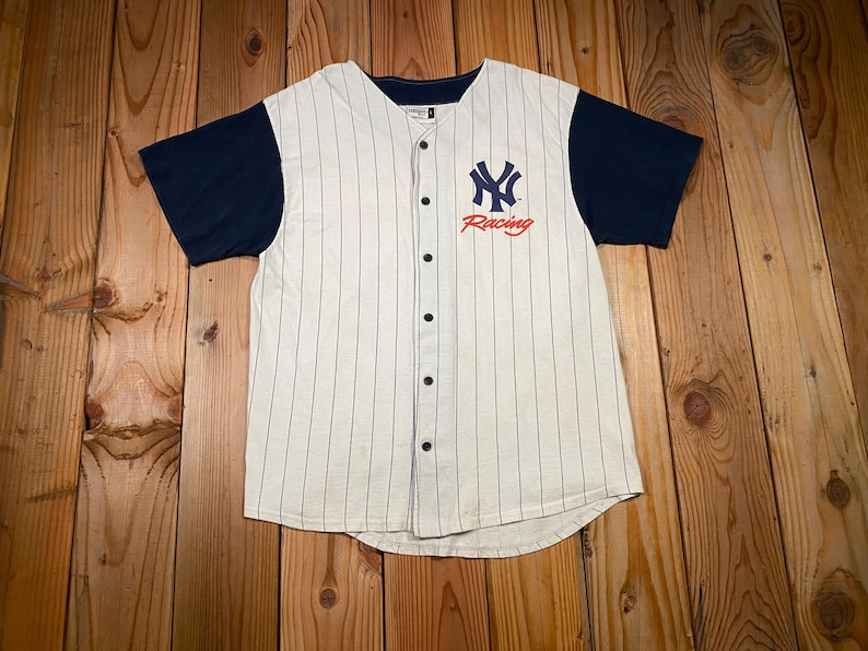 Peut inclure: Un maillot de baseball &agrave; manches courtes avec un corps couleur cr&egrave;me &agrave; fines rayures verticales et des manches bleu marine unies. L'avant pr&eacute;sente un logo NY entrelac&eacute; bleu marine au-dessus du mot Racing en &eacute;criture rouge, avec une fermeture boutonn&eacute;e.