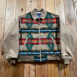May include: A tan jacket featuring a front panel with a geometric pattern in green, orange, red, and blue. The jacket has a full-length front zipper, a tan collar, solid tan sleeves, and a ribbed knit hem and cuffs. A Pendleton label is visible.