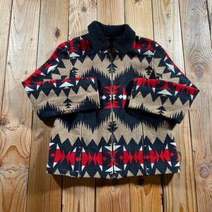 May include: A zip-up jacket featuring a geometric pattern in tan, black, red, and white. The jacket has long sleeves, a black sherpa-style collar, and a full-length front zipper closure. The fabric displays a repeating triangular and diamond motif.