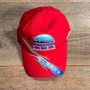 Op de afbeelding: Een felrode honkbalpet met het geborduurde logo van de Top Eliminator Club National Hot Rod Association. Het ontwerp bevat een blauwe verloopafbeelding, zilveren golvende lijnen en het jaartal 2003 gedrukt op de voorste klep.