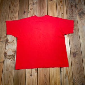 May include: A solid red short-sleeved t-shirt featuring a crew neckline. The garment is displayed flat, showcasing a plain, vibrant red fabric throughout the entire front surface of the shirt, with no additional patterns, graphics, or text visible.