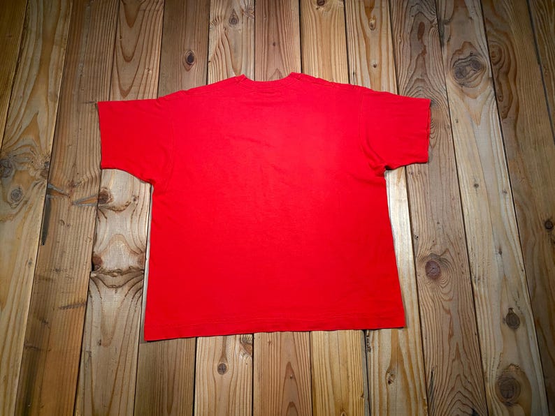 May include: A solid red short-sleeved t-shirt featuring a crew neckline. The garment is displayed flat, showcasing a plain, vibrant red fabric throughout the entire front surface of the shirt, with no additional patterns, graphics, or text visible.