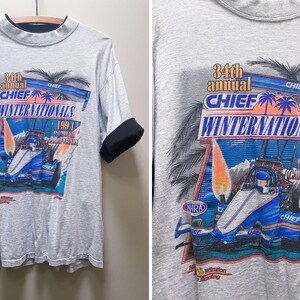May include: A gray t-shirt with a graphic of a race car and palm trees. The text on the shirt reads "34th annual CHIEF WINTERNATIONALS 1994 POMONA CALIFORNIA".