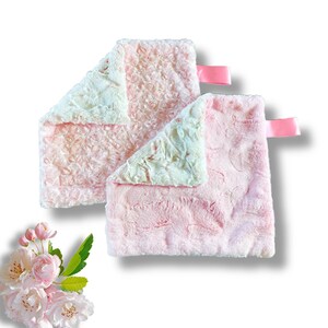 May include: Two pink and white baby blankets with satin ribbon ties. The blankets are soft and plush with a rose pattern on one side and a solid pink color on the other.
