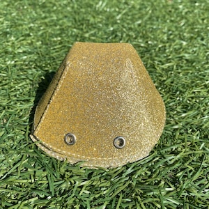 Könnte beinhalten: Ein goldfarbener, glitzernder Hut in Kegelform mit zwei silbernen Ösen.