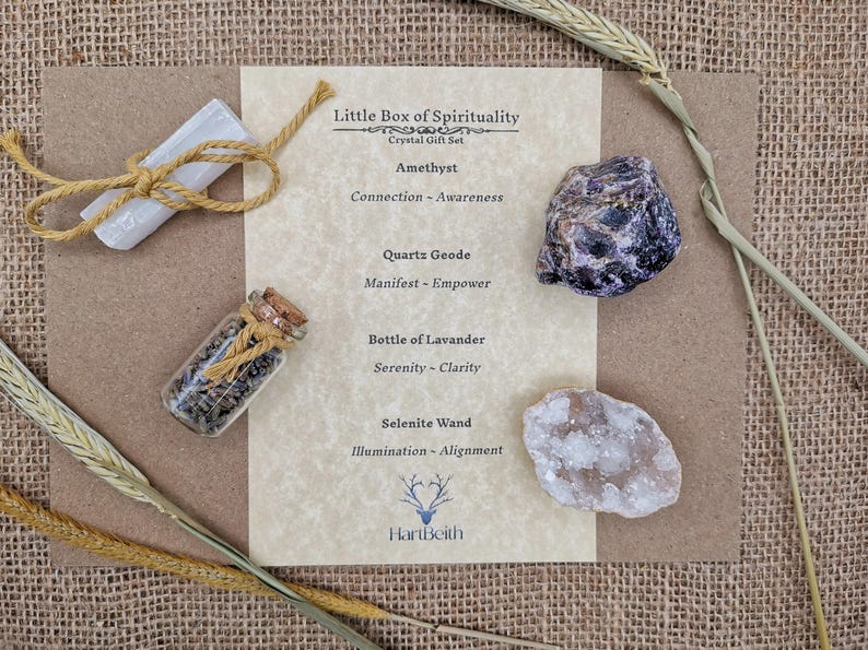 May include: A set of crystals and a bottle of lavender for spiritual practices. The set includes amethyst, quartz geode, selenite wand, and a bottle of lavender. The crystals are arranged on a piece of paper with the text "Little Box of Spirituality" and "Crystal Gift Set".