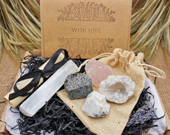 May include: A gift box filled with crystals and a selenite wand. The box is lined with black shredded paper and includes a small burlap bag with rose quartz, clear quartz, and a black stone. The box has a label that says "With Love".