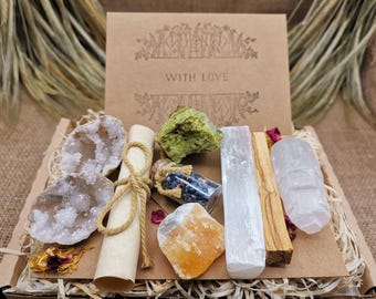 May include: A gift box filled with crystals and other spiritual items. The box includes a clear quartz crystal, a selenite crystal, a palo santo stick, a piece of orange calcite, a small bottle of blue crystals, a rolled up piece of parchment, and a green crystal. The box is decorated with dried flowers and the words "With Love" are printed on the top.