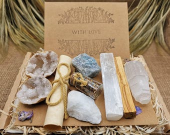 May include: A gift box filled with crystals and other spiritual items. The box contains a clear quartz crystal, a selenite wand, a palo santo stick, a small bottle of herbs, a rolled up piece of parchment, and a geode. The box is decorated with a brown paper label that says "With Love".
