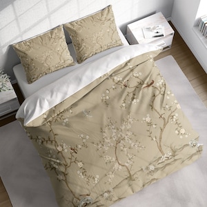 May include: Beige duvet cover with a floral pattern featuring delicate branches, white blossoms, and small birds. The duvet cover has a white border and is shown with two matching pillowcases.