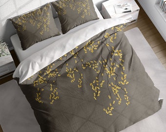 May include: A bed set featuring a duvet cover and two pillowcases. The set has a dark gray background with a pattern of yellow floral branches. The pillowcases and the duvet cover are arranged on a white bed.