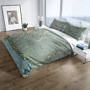 Puede incluir: Una funda n&oacute;rdica azul y blanca con un estampado floral que presenta un &aacute;rbol con flores blancas y p&aacute;jaros. La funda n&oacute;rdica est&aacute; en una cama con dos fundas de almohada a juego.