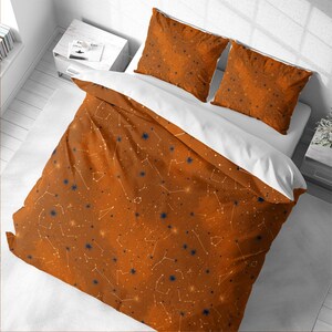 May include: A burnt orange duvet cover and two matching pillowcases featuring a white and dark blue celestial pattern of stars and constellations. The bedding set has a solid white underside and is displayed on a bed with a white frame.