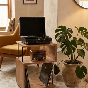 May include: A wooden two-tier storage unit with a black metal frame. The top shelf holds a black portable record player with a vinyl record. The middle shelf holds a brown vintage-style radio. The bottom shelf stores vinyl records.