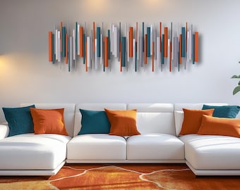 Op de afbeelding: Een horizontale wandsculptuur bestaande uit talrijke verticale cilindrische staven van verschillende lengtes en diameters. De staven hebben een kleurenpalet van levendig oranje, diep petrol, metallic zilver en lichtgrijs, gerangschikt in een dicht patroon.