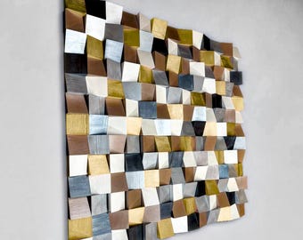 Puede incluir: Una pieza de arte mural cuadrada compuesta por numerosos bloques de madera pequeños e individuales dispuestos en una cuadrícula. Los bloques presentan profundidades variables y están acabados en una paleta de tonos oro metálico, plata, negro, blanco y madera natural.