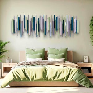 May include: A bedroom scene featuring a bed with green bedding and pillows. Above the bed is a wall art piece composed of vertical wooden slats in shades of green, blue, and gray. A potted plant and a hanging plant add to the room's decor.