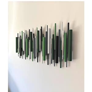 May include: Abstract wall art comprising vertical cylinders in shades of green, grey, black, and silver. The cylinders are mounted on a white wall, creating a modern aesthetic. The cylinders vary in length and diameter, offering a minimalist design.