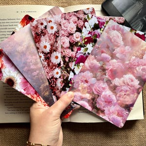 May include: A selection of floral bookmarks featuring designs of pink roses, daisies, and abstract floral patterns. The bookmarks are displayed over an open book and an e-reader, set against a neutral backdrop.