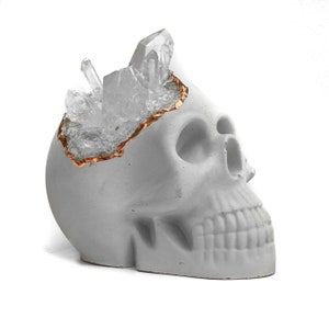 May include: A white concrete skull with a gold-rimmed opening filled with clear quartz crystals.