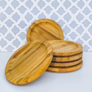 May include: A stack of six round, natural bamboo coasters. The coasters are smooth and have a slightly raised edge.