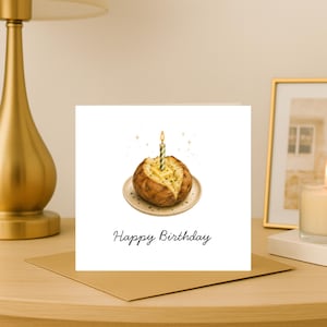 May include: A square greeting card with a white background featuring a centred illustration of a baked potato on a small plate, topped with a melting pat of butter and a single lit birthday candle. The text Happy Birthday is printed below.
