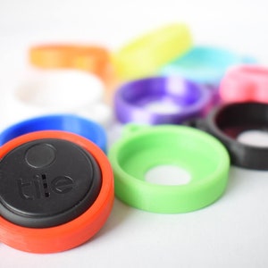 以下が含まれることがあります： カラフルなTileトラッカーと保護ケースのコレクション。メインのトラッカーは赤と黒で、「tile」の文字が印刷されています。他のケースは、緑、青、ピンクなど、さまざまな色があります。